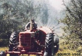 picture of man on tractor using agricultural pesticide sprayer on orchard trees