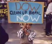 picture of young boy carrying sign that says 'Dow clean up Bhopal NOW'; click to go to video page; opens in new window